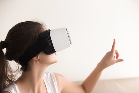 Curious woman in VR headset touching virtual world by finger, enjoying 3d tour, interacting with augmented reality digital interface, making purchases online, study in goggles, headshot, copy spaceの写真素材