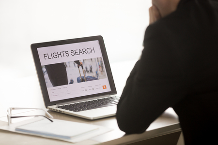 Businessman using laptop for searching cheap low cost business flight, choosing airfare deal, comparing trip prices, booking airplane ticket online on web service, focus on screen, close up back viewの写真素材