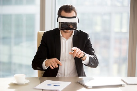 Businessman in vr headset goggles working in augmented reality at workplace. Young office worker or entrepreneur immersed in virtual reality, using innovative technology, managing business projects.の写真素材