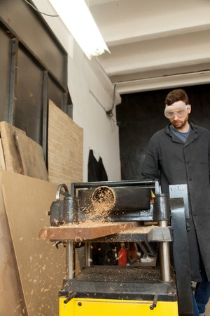 Joiner works at machine tool in workshop. Carpenter reduce wooden board thickness at planer machine....