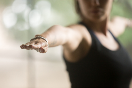 Young sporty woman practicing yoga at home, standing in Warrior Two exercise, Virabhadrasana II pose, working out, wearing sportswear, black top, indoor closeup, studio background, focus on handの写真素材