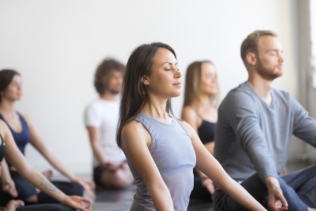 Group of young people, sporty students practicing yoga lesson with instructor, sitting and...