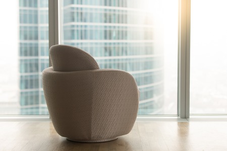 Modern office room with empty designer chair near full length big panoramic glass window and urban city skyscraper outside, luxury contemporary apartment interior, furniture for relaxation, rear viewの写真素材