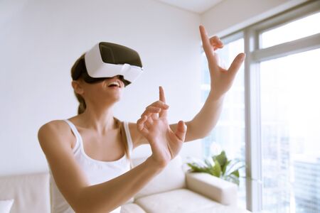 Young excited woman wearing VR headset touching objects in virtual world, using goggles mobile...