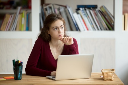 Thoughtful young female entrepreneur in front of laptop. Casual businesswoman thinking about possibility of seeking new business opportunities. Freelance small business owner daydreaming about future.の写真素材