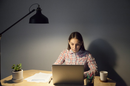 Young adult employee making late evening report on laptop computer, deep in thoughts, current result showing growthの写真素材