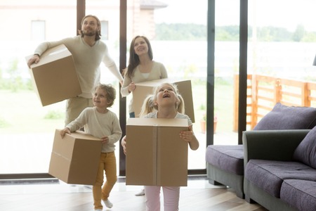 Excited family with children coming into new home on moving day, happy kids and parents looking around holding cardboard boxes entering in big house, buying real estate, mortgage loan, relocationの写真素材
