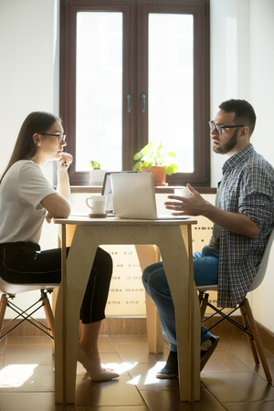 Young businesswoman and businessman sitting at meeting and discussing new working concept. Millennial employees negotiating in office. Vertical imageの写真素材