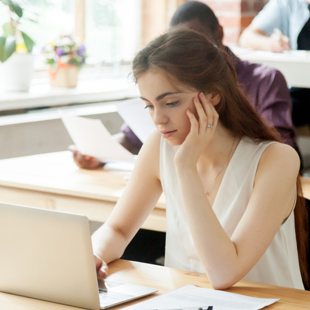 Young attractive woman working on laptop in coworking space, focused freelancer using computer in workspace environment or student passing exam in classroom with multinational people aroundの写真素材
