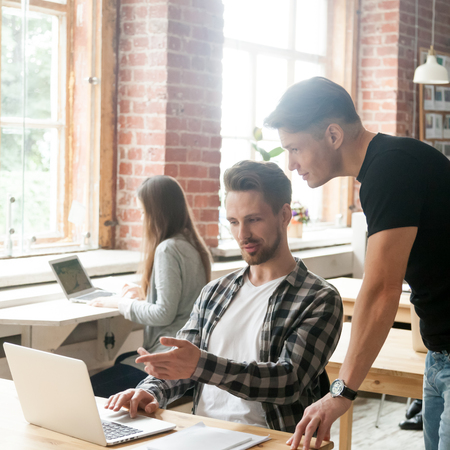 Businessman pointing at laptop screen talking to colleague discussing project in coworking space, intern asking for team leader help working together in shared office, coworkers teamwork at workplaceの写真素材