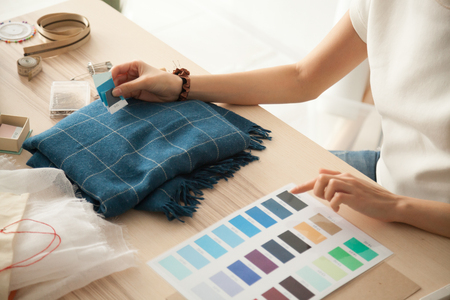 Female fashion designer holding color samples choosing fabric textile blue shades at workplace, dressmaker or tailor working at desk pointing at set palette making choice selection, close up viewの写真素材