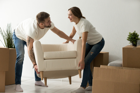 Young couple carrying chair together, house improvement, modern furniture in new home concept, man and woman moving into own flat after relocation furnishing living room, remodeling and renovationの写真素材
