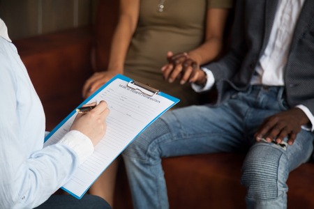 Doctor or psychologist filling medical patient information form holding clipboard consulting african...