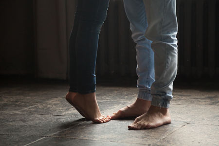 Barefoot girl standing on tiptoe to hug her man at home, sweet cute romantic couple kissing concept, male and female legs feet wearing jeans close up view, warm floor heating, femininity and delicacyの写真素材