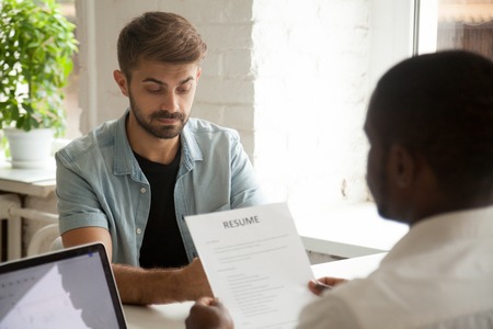 Stressed caucasian applicant feels worried while african hr employer reading resume, stress at job...