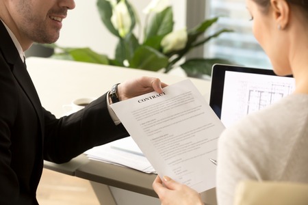 Male credit expert or real estate agent offering female client sign contract to buy apartments or house. Woman reading housing loan agreement and listening realtor, contractor representative adviseの写真素材