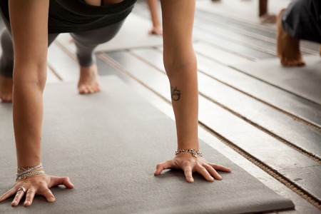 Close up of female arms, yogi woman and group of sporty people practicing yoga, standing in Plank pose, doing Push ups or press ups exercise, working out, weight loss training lesson, close up, studioの写真素材