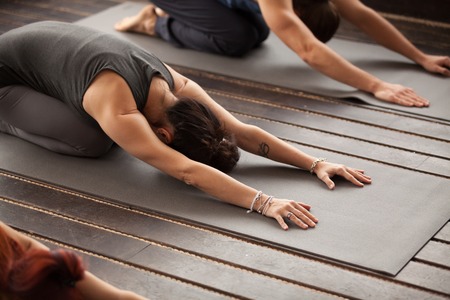 Group of young sporty people practicing yoga lesson with instructor, stretching in Child exercise,...