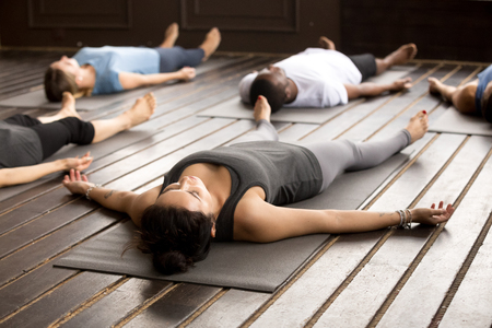 Group of young afro american and caucasian sporty people practicing yoga lesson lying in Dead Body pose, Savasana exercise, working out, resting after practice, indoor close up, studioの写真素材