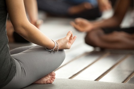 Young sporty woman practicing yoga lesson sitting in Sukhasana exercise, Easy Seat pose with mudra gesture, working out, female arms with wrist bracelets close up, studio