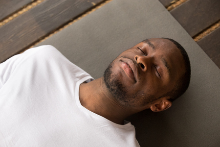Photo of young black man lying in Dead Body exercise or Corpse pose with his eyes closed, Savasana pose, working out, resting after practice, close up, studio, top view. Healthy lifestyle conceptの写真素材