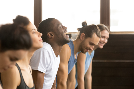 African man beginner laughing having fun trying to do yoga pose, push ups plank or stretching in upward facing dog exercise at group training class with multiracial diverse people, closeup side viewの写真素材
