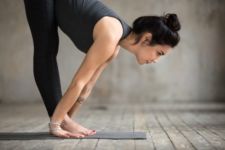 Young woman practicing yoga, doing Ardha uttanasana exercise, Standing Half forward pose, working...