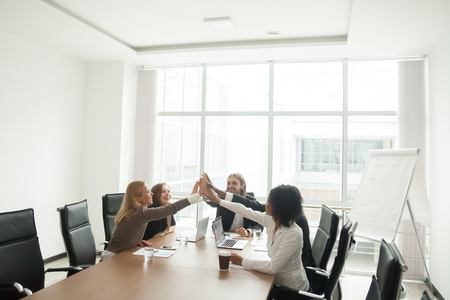 Happy business people giving high five building successful team in office sitting at meeting table, multiracial motivated group celebrating victory join hands together, unity help support in teamworkの写真素材
