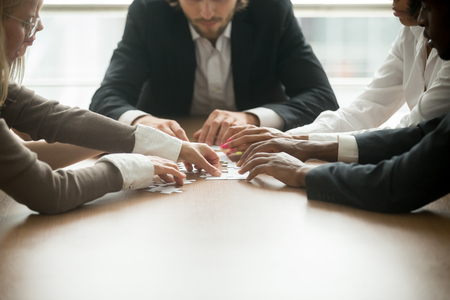 Multiracial business team assembling jigsaw puzzle, diverse group of businesspeople playing board game together joining pieces on office desk, help support in teamwork and corporate unity conceptの写真素材