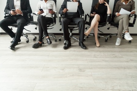 Diverse business people waiting in queue holding smartphones and resumes, multiracial men and women sitting in row anticipating job interview, human resources, employment hiring concept, copy spaceの写真素材