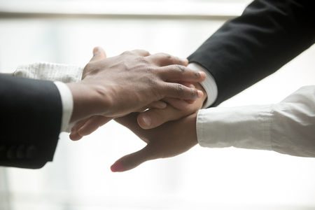 African and caucasian partners join hands in pile together, motivated multiracial business team promising help and support, engagement or unity in collaboration, commitment in teamwork, close up viewの写真素材