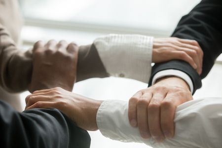 Four multiracial business people holding each others wrists, diverse partners join hands together as concept of reliable support in team, strength, power and unity in collaboration, close up viewの写真素材