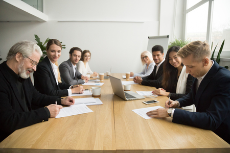 Senior and young businessmen sign contracts at group multiracial meeting, experienced investor buying startup making partnership deal after successful negotiation putting signature on business papersの写真素材