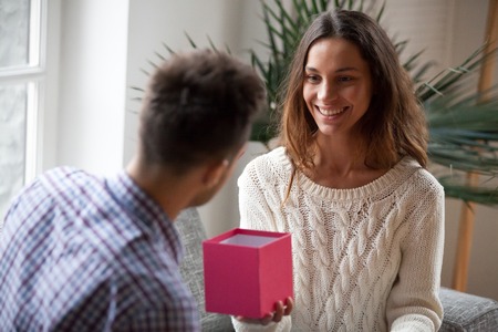 Young wife making present giving open pink box to husband, smiling happy woman congratulating man with birthday holding gift, loving girlfriend presenting romantic surprise to boyfriend on occasionの写真素材