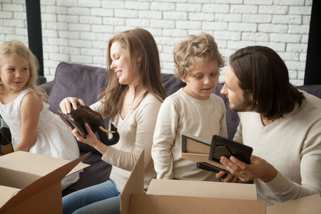 Family with kids son and daughter unpacking boxes together talking on moving day settling in new home, happy children helping smiling parents to pack in living room on sofa preparing for relocationの写真素材