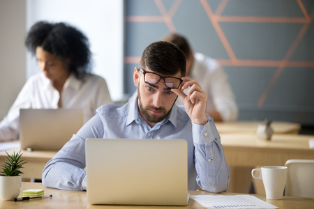 Shocked businessman stunned by online news raising glasses to look at laptop in coworking office, stock broker surprised by market changes watching video or reading information on computer screenの写真素材