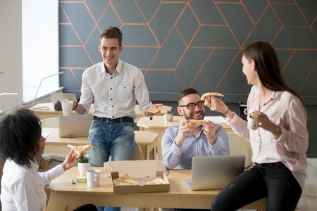 Friendly diverse team talking and laughing eating pizza together, happy colleagues sharing meal, multiracial coworkers group enjoying lunch at break, good relations and office food delivery conceptの写真素材