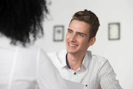 Smiling interested male hr manager interviewing applicant, professional friendly recruiter makes good first impression of job seeker, happy millennial businessman looking at female partner at meetingの写真素材