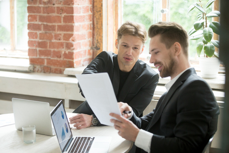 Young male manager explaining details of financial project to his business colleague while working with charts and diagrams on laptops. Horizontal shot, selective focus. Coworking and partnershipの写真素材