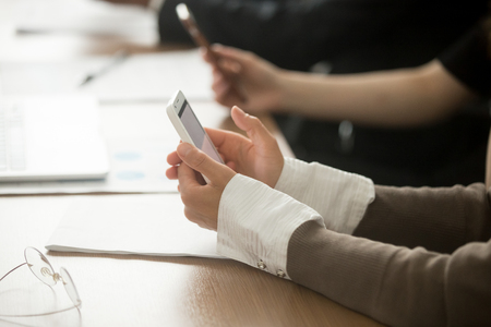 Female hands holding mobile phone at office corporate meetingの写真素材