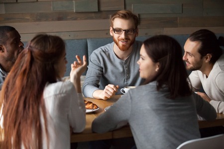 Diverse young people talking and having fun together in cafe, girls chatting sharing coffeehouse table with multiracial friends, multi-ethnic millennials enjoying pleasant discussion in public placeの写真素材