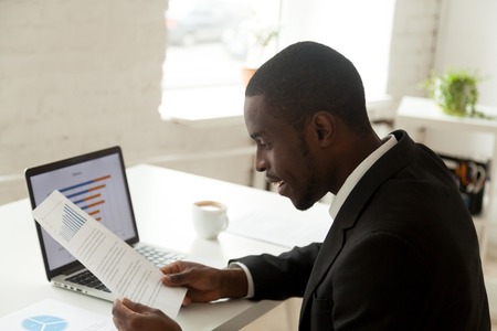 Excited African American manager reading company financial report, happy about raising rates and...