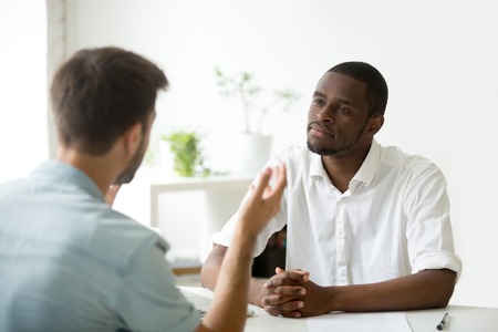 African American employer listening attentively to caucasian job applicant talking at work interview, being friendly and interested to candidate. Concept of recruiting, employment, hiringの写真素材