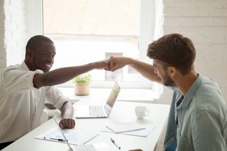 Two workers giving fist bump, celebrating business achievement with arms up, congratulating with successful deal, shared accomplishment. Concept of teamwork, cooperation, collaboration, respect, helpの写真素材