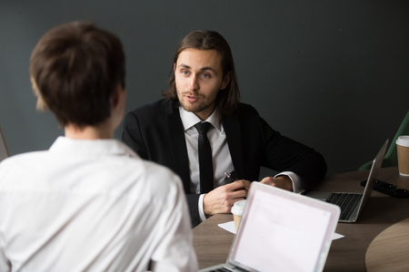 Back view from shoulder of businesswoman listening to millennial male partner talking during business meeting in boardroom, businessman explaining project strategyの写真素材
