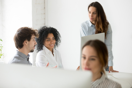 Multiracial colleagues looking at laptop screen coworking in shared open space, female team leader controlling processの写真素材