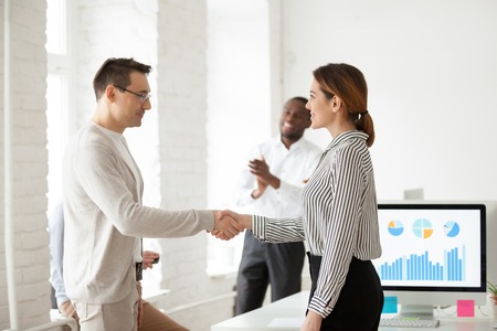 Middle aged male CEO shaking hand of proud female worker, congratulating with high work achievements, successful project during meeting, colleagues applauding behind.の写真素材