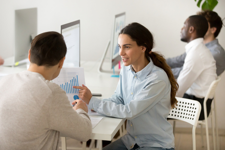 Smiling female worker showing financial graph to male client or colleague, explaining company statistics, talking about sales growth, sharing ideas of business successful strategy.の写真素材