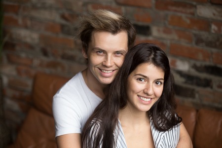 Family portrait of millennial beautiful happy couple looking to camera, loving husband hugging wife...