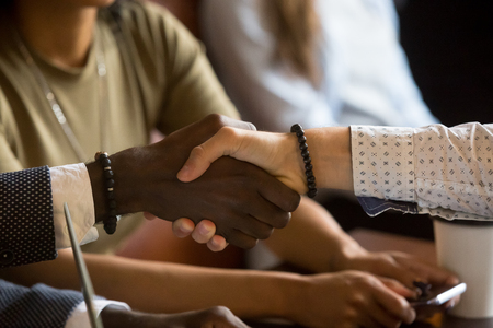 Close up of multiracial handshake at business meeting closing deal, African and Caucasian men shaking hands greeting congratulating with successful agreement, signing contract. Unity support conceptの写真素材